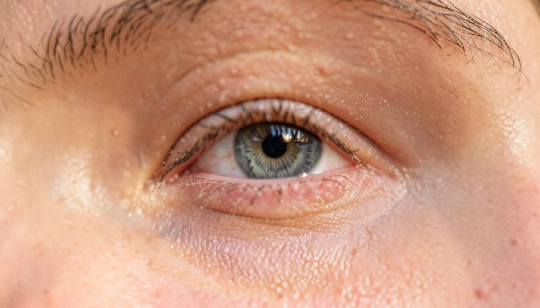 Close-up of a natural eye with a visible hooded crease, warm skin tones, soft daylight, gentle and honest mood