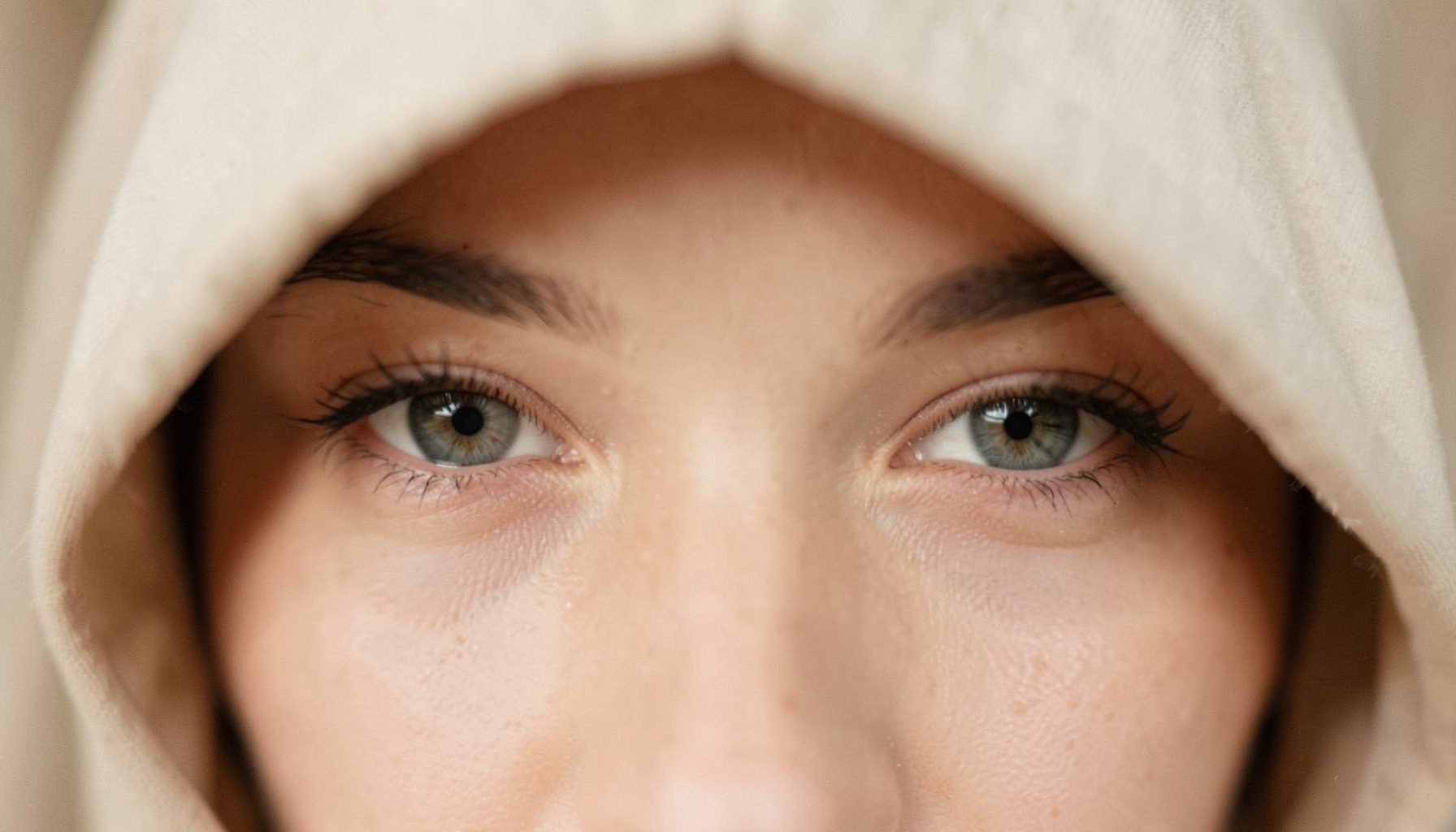 Soft close-up of a pair of eyes with a subtle hooded shape, warm neutral tones, gentle diffused lighting, calm and elegant mood