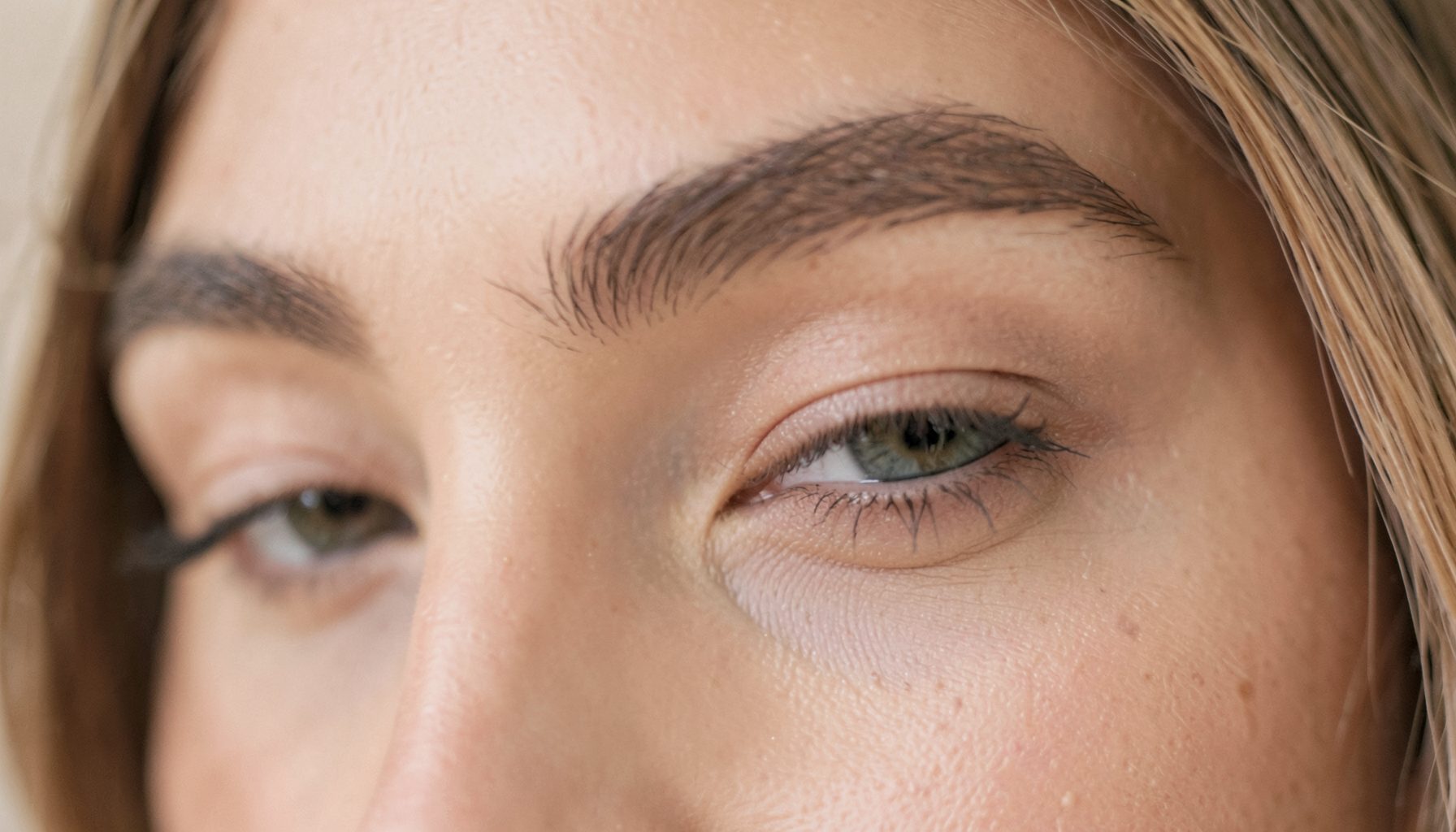 Soft close-up of a woman's eye area with gently hooded eyelids, warm neutral tones, diffused natural light, calm and elegant mood