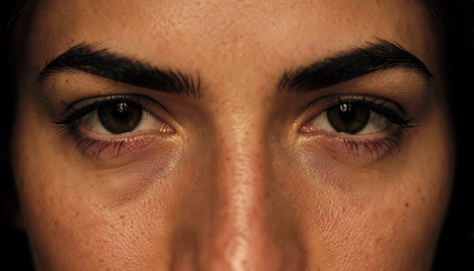 Close-up of a pair of deep-set eyes with heavy brow bones and softly draped eyelids, warm amber and charcoal tones, moody and intimate mood